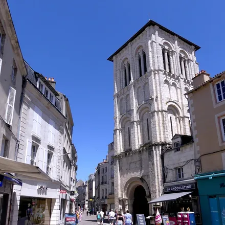 Le clocher-porche de l’église Saint-Porchaire, au fond d’une rue piétonne bordée de maisons, sous un ciel bleu.